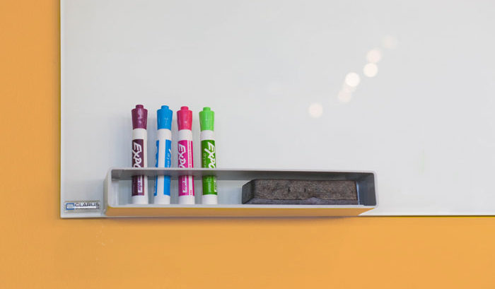 four flourescent expo markers standing up against a clean whiteboard against a light orange wall