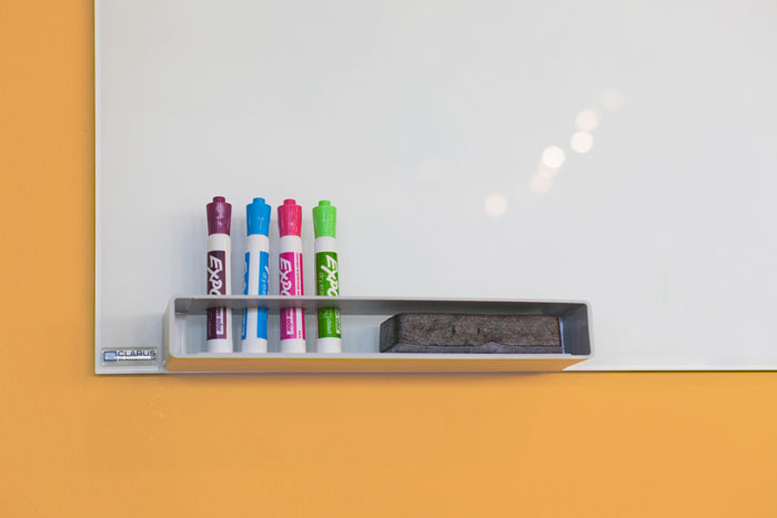 four flourescent expo markers standing up against a clean whiteboard against a light orange wall
