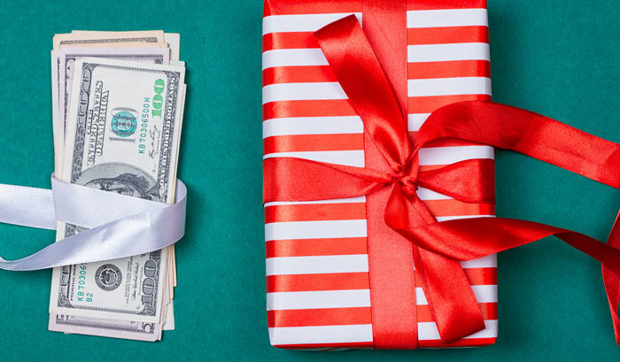 stack of cash wrapped in ribbon next to holiday gift to symbolize a holiday bonus