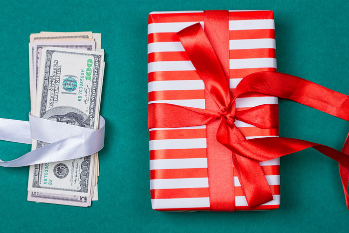 stack of cash wrapped in ribbon next to holiday gift to symbolize a holiday bonus