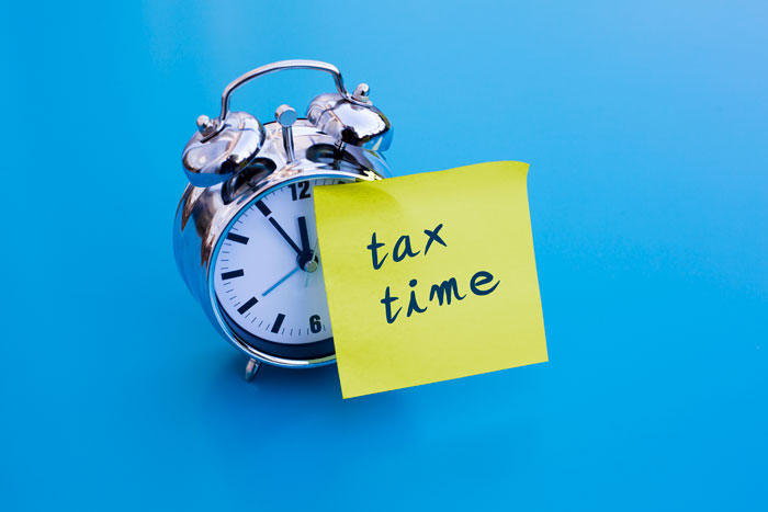 image of alarm clock with tax time written on a yellow sticky note on it