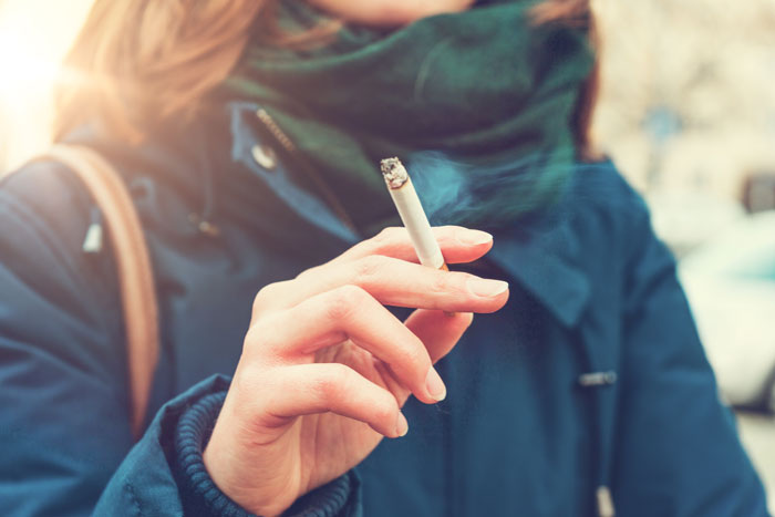 woman in work parking lot in a coat and scarf smoking a cigarette