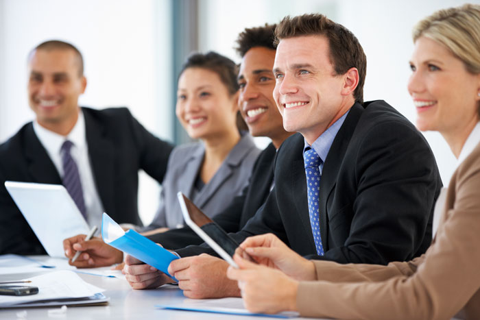group of employees in business suits smiling and listening to someone speaking