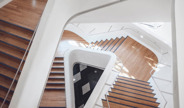 downward focused image of wooden stairs twisting at different levels with white walls and light