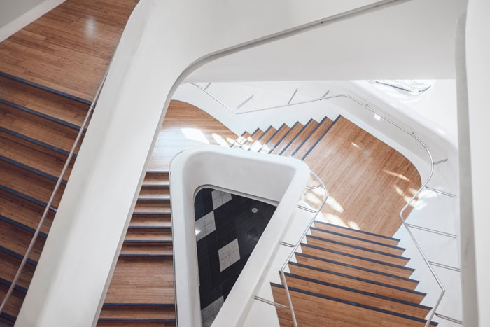 downward focused image of wooden stairs twisting at different levels with white walls and light