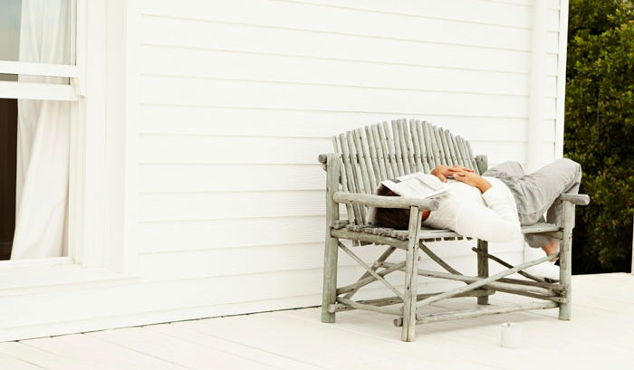 businessman sick and sleeping on home wicker bench with newspaper over head
