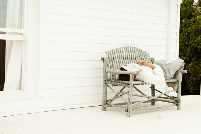 businessman sick and sleeping on home wicker bench with newspaper over head