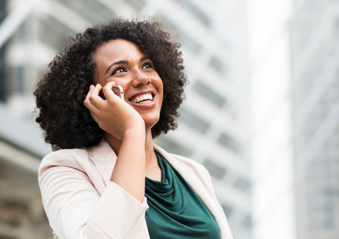 Young biracial woman in business attire smiling on a cell phone on an overcast day