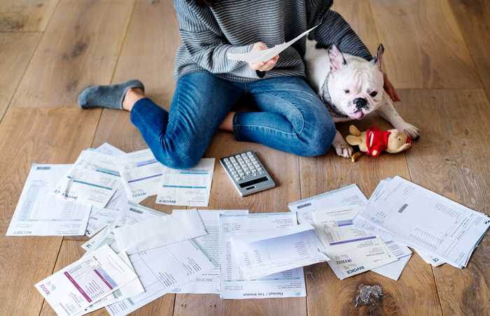 young person sitting on floor with dog looking at piles of scattered bills