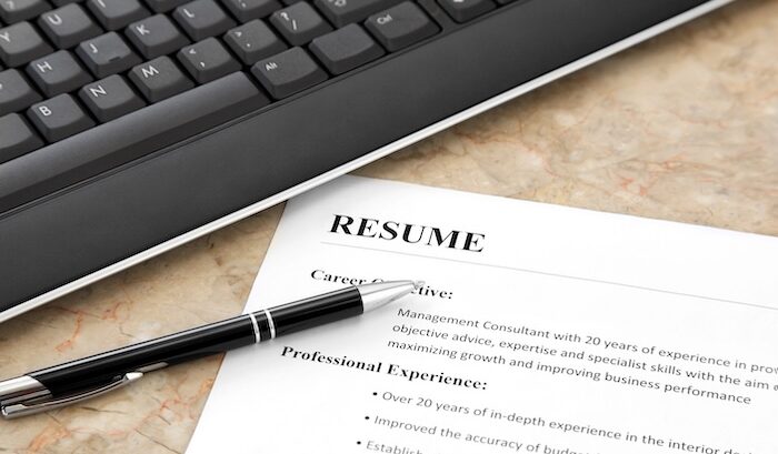 A close-up of a printed resume on a desk, with a black pen resting on the page and a computer keyboard partially visible in the background.